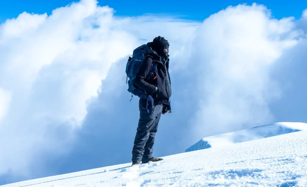 Zara Tanzania Adventures mountain guide standing on the snowy summit of Mount Kilimanjaro, surrounded by clouds at Africa’s highest peak.