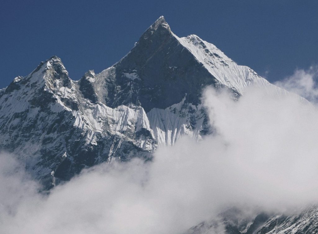 Snow-covered Annapurna peak with rugged slopes under a pale sky