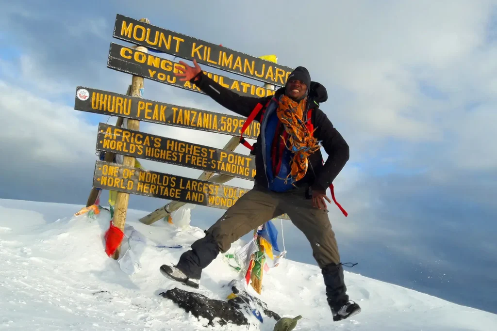 Zara Tanzania Adventures mountain guide celebrating at Uhuru Peak, the summit of Mount Kilimanjaro, standing at 5,895 meters above sea level.