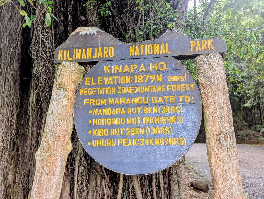 Kinapa Headquarters sign at Kilimanjaro National Park showing elevation and distances from Marangu Gate to huts and Uhuru Peak